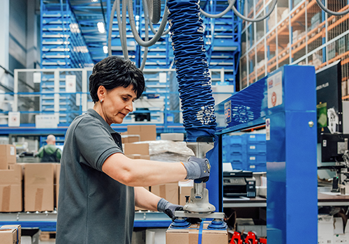 Frau arbeitet in modernem Lager und hebt mit einer speziellen Vorrichtung ein zu versendendes Paket an